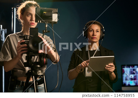 Waist up portrait of two women working in video production crew and operating camera on set 114758955