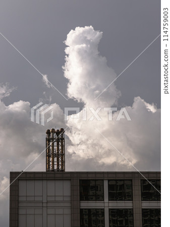 Four chimneys on the flat roof off a big building with fluffy white clouds on sky in the background. Four chimneys on the flat roof off a big building with fluffy white clouds on sky in the background. 114759003