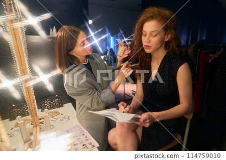 Portrait of young actress preparing for show backstage in theater with vanity lights lens flare Portrait of young actress preparing for show backstage in theater with vanity lights lens flare 114759010