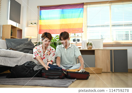 Cheerful gay male couple preparing clothes into luggage for their summer vacation Cheerful gay male couple preparing clothes into luggage for their summer vacation 114759278