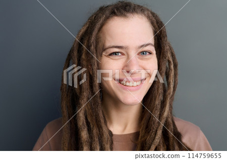 Minimal close-up portrait of smiling young woman with long dreadlocks looking at camera on grey Minimal close-up portrait of smiling young woman with long dreadlocks looking at camera on grey 114759655