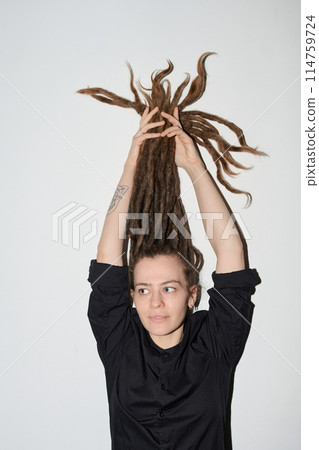 Vertical portrait of funky Caucasian woman with long dreadlocks standing against white wall shot with flash 114759724