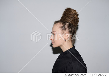 Minimal side view portrait of Caucasian woman with dreadlocks in bun hairstyle standing on white background shot with flash copy space Minimal side view portrait of Caucasian woman with dreadlocks in bun hairstyle standing on white background shot with flash copy space 114759727