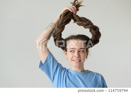 Minimal portrait of playful Caucasian woman with long dreadlocks holding hair up and smiling copy space 114759794