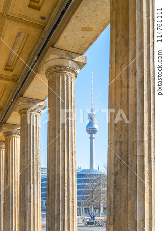 The Berlin TV Tower stands tall, framed by the classical columns of a nearby historical building on a clear day. Berlin, Germany 114761111