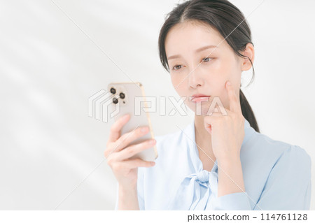 一個帶著思考表情操作智慧型手機的女人 一個帶著思考表情操作智慧型手機的女人 114761128