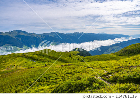 A hiker explores the lush trails of the Austrian Alps with a majestic mountainous backdrop and low-hanging clouds. Salzach Valley, Hohe Tauern, Austria 114761139