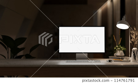 A white-screen computer mockup and a dim light from a lamp on a table in a modern dark office. A white-screen computer mockup and a dim light from a lamp on a table in a modern dark office. 114761791