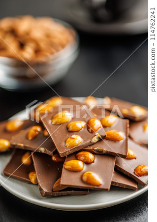 Broken chocolate bar with almonds on plate on black table. Broken chocolate bar with almonds on plate on black table. 114762241