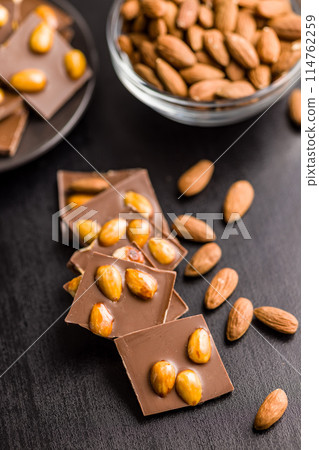 Broken chocolate bar with almonds on black table. Broken chocolate bar with almonds on black table. 114762259