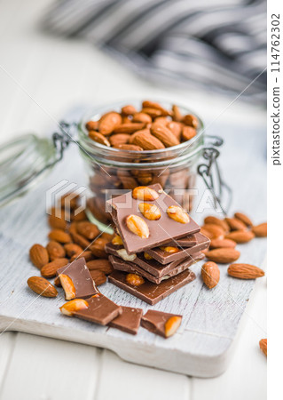 Broken chocolate bar with almonds on kitchen table. 114762302