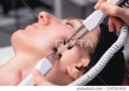 Close-up of a woman receiving an electric neck massage with equipment in a beauty salon. Used for therapy with a multifunctional electro massage device 114762420