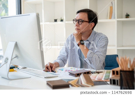 An expert Asian senior male interior designer is focused on checking the design on his computer. An expert Asian senior male interior designer is focused on checking the design on his computer. 114762698