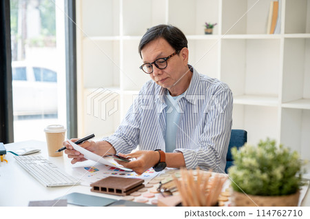 A satisfied senior Asian male interior designer is checking the building material on samples. 114762710