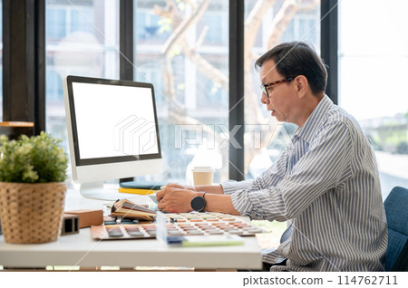 An experienced Asian male interior designer or architect is working on his project in the office. 114762711