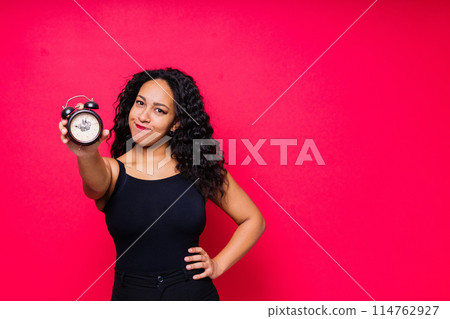 Smiling young african american woman posing isolated on red background with clock 114762927