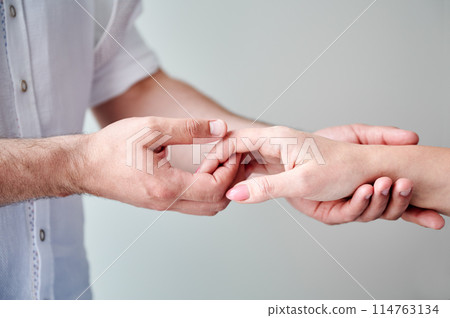 Close up of two hands engaging in delicate touch. Man's and woman's hands on white neutral background. Husband holding hand of his lovely wife. Concept of affection, support, and mutual respect. 114763134