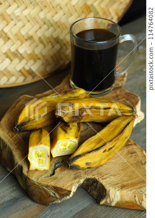 a halved steamed banana and a whole banana on a wooden cutting board 114764082