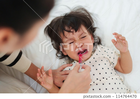 mother feeding liquid medicine to baby girl by syringe. sick crying toddler 114764470