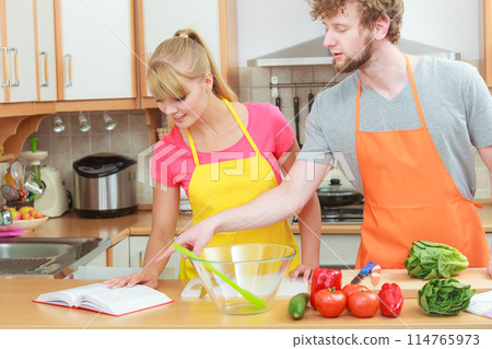 Couple cooking in kitchen reading cookbook 114765973