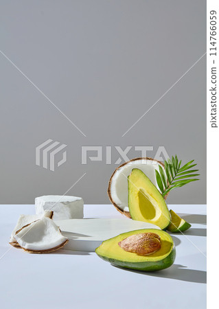 Frontal shot photo on light gray background with coconut and avocado ingredient, a circular platform with blank space placed in center of white table top for displaying product has natural origin 114766059