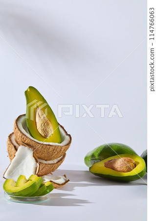 Vertical photo with white texture, some fresh avocado flat lay on white table next to dry coconut and a dish of avocado slices. Vacant space in center for adding elements of designing, frontal shot Vertical photo with white texture, some fresh avocado flat lay on white table next to dry coconut and a dish of avocado slices. Vacant space in center for adding elements of designing, frontal shot 114766063