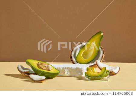 A light color table top displaying fresh fruits ingredient for manufacturing organic beauty care product consist of avocado and coconut with a blank white podium in center. Vacant space for design A light color table top displaying fresh fruits ingredient for manufacturing organic beauty care product consist of avocado and coconut with a blank white podium in center. Vacant space for design 114766068