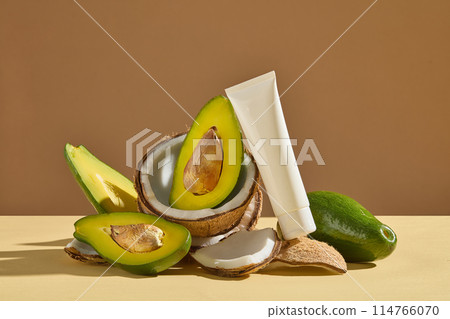 Brown color texture against a blank label cosmetic tube leaning on a small pile of fruit including avocado and coconut. Frontal shot photo with blank space for adding elements of design 114766070