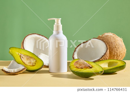 A pump bottle without label decorated with halves of coconut and avocado on beige surface. Green background. Empty label for cosmetic product mockup A pump bottle without label decorated with halves of coconut and avocado on beige surface. Green background. Empty label for cosmetic product mockup 114766431