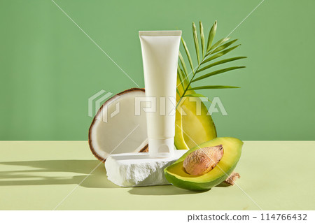 Against the green background, an unlabeled tube displayed on a stone podium with halves of coconut and avocado. White cosmetic tube for face cream, cleanser, body lotion or shampoo Against the green background, an unlabeled tube displayed on a stone podium with halves of coconut and avocado. White cosmetic tube for face cream, cleanser, body lotion or shampoo 114766432