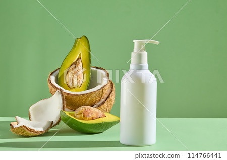 Concept for natural cosmetic products advertising with a pump bottle decorated with a stack of avocado and coconuts. Cosmetics, products for care and personal hygiene concept Concept for natural cosmetic products advertising with a pump bottle decorated with a stack of avocado and coconuts. Cosmetics, products for care and personal hygiene concept 114766441