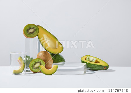 Glass podium in round shaped decorated with avocado and kiwi cut in some slices and halves. White background. Laboratory experience and research concept 114767348