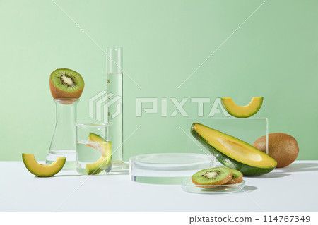 Green background features types of glassware, an empty podium and fresh kiwis with avocados. Fresh fruit concept. Chemical liquid for research and analysis in the laboratory 114767349