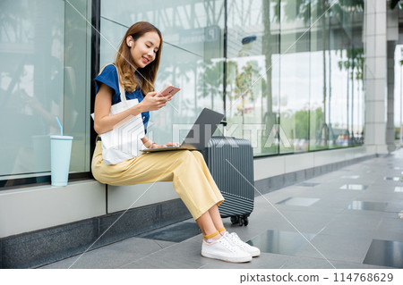 A female blogger works remotely from a train station, using her laptop to share her travel experiences with the world. She's always on the go, but her work never stops. digital nomad lifestyle. 114768629