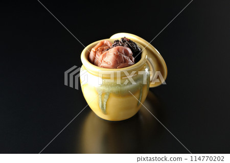 Pickled plums and red shiso in a jar photographed against a black background Pickled plums and red shiso in a jar photographed against a black background 114770202