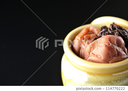 Pickled plums and red shiso in a jar photographed against a black background Pickled plums and red shiso in a jar photographed against a black background 114770222