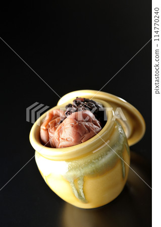 Pickled plums and red shiso in a jar photographed against a black background Pickled plums and red shiso in a jar photographed against a black background 114770240
