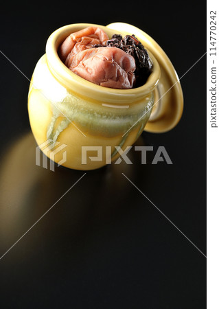 Pickled plums and red shiso in a jar photographed against a black background Pickled plums and red shiso in a jar photographed against a black background 114770242