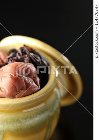 Pickled plums and red shiso in a jar photographed against a black background Pickled plums and red shiso in a jar photographed against a black background 114770247