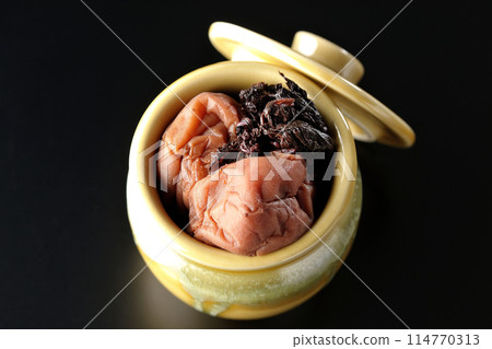 Aerial view of pickled plums and red shiso in a jar against a black background Aerial view of pickled plums and red shiso in a jar against a black background 114770313