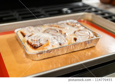 Just out of the oven, cinnamon rolls cool on a silicone baking mat, their icing glistening under the kitchen lights. Just out of the oven, cinnamon rolls cool on a silicone baking mat, their icing glistening under the kitchen lights. 114770455