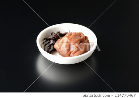 黑色背景下小盤子上的紅紫蘇和醃李子的照片 114770467