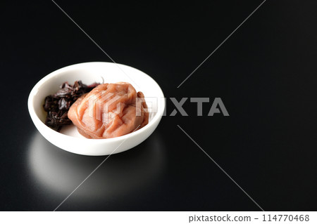 Red shiso and pickled plums served on a small plate photographed against a black background Red shiso and pickled plums served on a small plate photographed against a black background 114770468