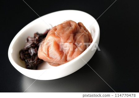 Red shiso and pickled plums served on a small plate photographed against a black background Red shiso and pickled plums served on a small plate photographed against a black background 114770478