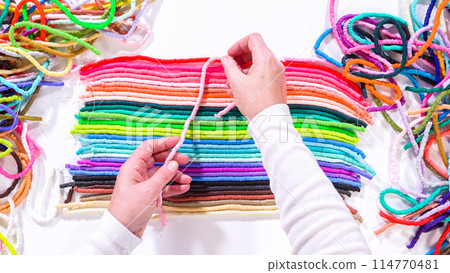 Flat lay. Hands touch a neatly organized rainbow of colorful, coiled clay bead strands against a contrasting white surface. 114770481