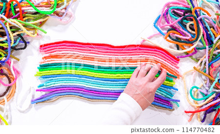 Flat lay. Hands touch a neatly organized rainbow of colorful, coiled clay bead strands against a contrasting white surface. 114770482
