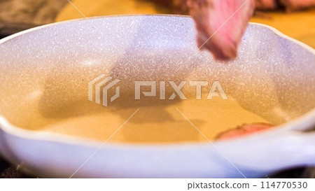 Tongs turning succulent medium-rare steak strips in a speckled ceramic skillet. 114770530
