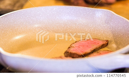 Tongs turning succulent medium-rare steak strips in a speckled ceramic skillet. Tongs turning succulent medium-rare steak strips in a speckled ceramic skillet. 114770545