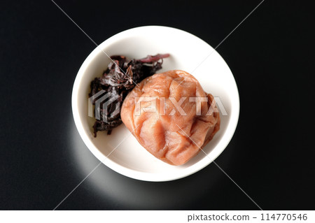 Aerial view of red shiso and pickled plums served on a small plate on a black background Aerial view of red shiso and pickled plums served on a small plate on a black background 114770546