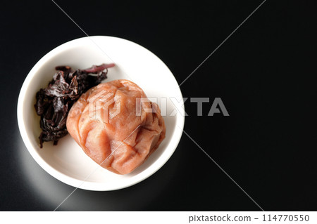 Aerial view of red shiso and pickled plums served on a small plate on a black background 114770550